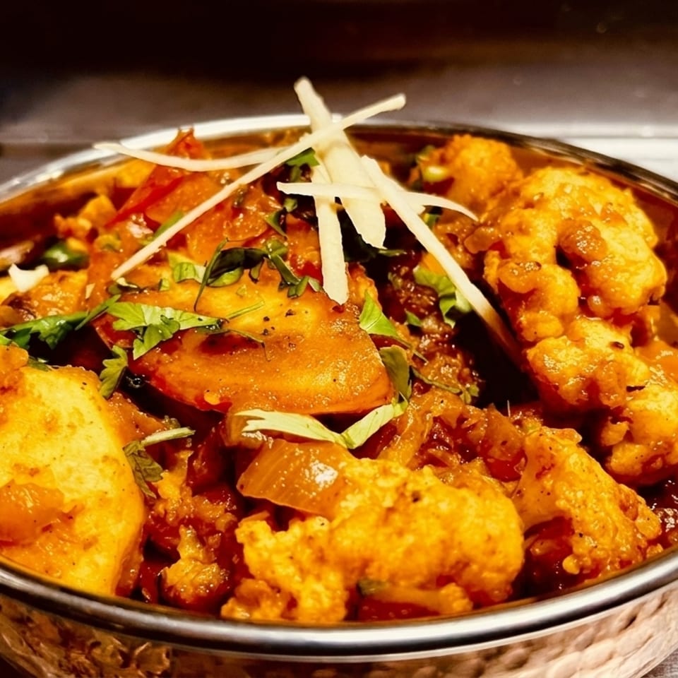 Close-up of a copper bowl filled with Indian curry, garnished with cilantro and ginger.