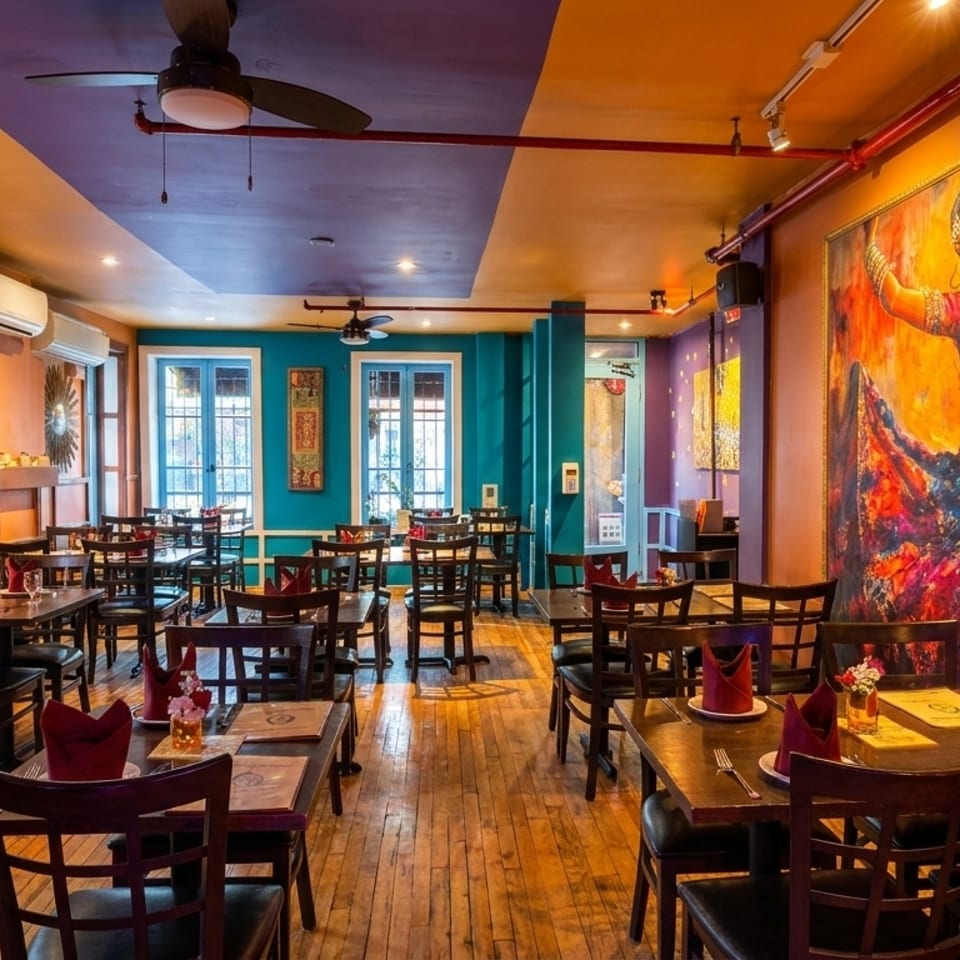 Vibrantly decorated restaurant interior with colorful walls, wooden tables, chairs, and a large painting of a dancer.