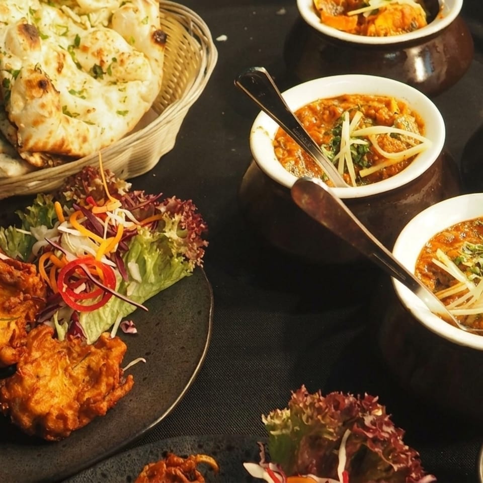 A tray of Indian food with naan bread, pakoras, and several bowls of curry.